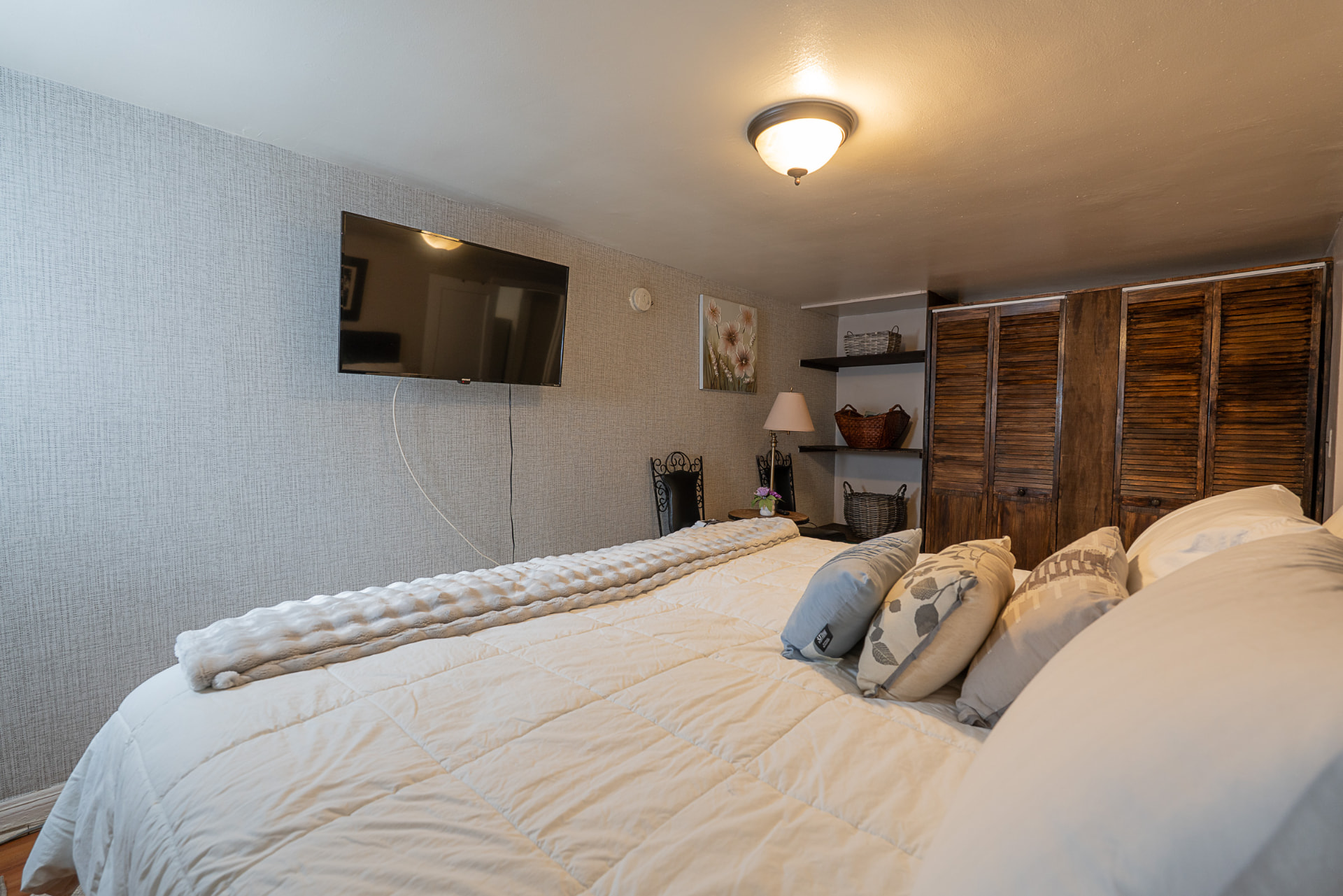 Bedroom with king bed, wall-mounted TV, wooden closet doors, and warm lighting