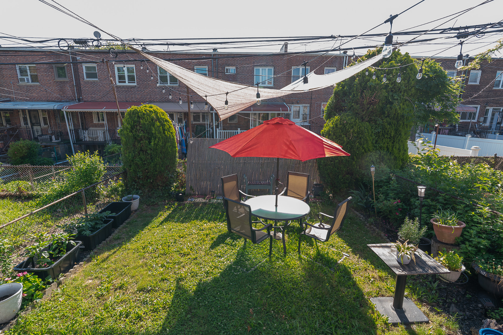 Private backyard garden with red patio umbrella, dining set, and string lights