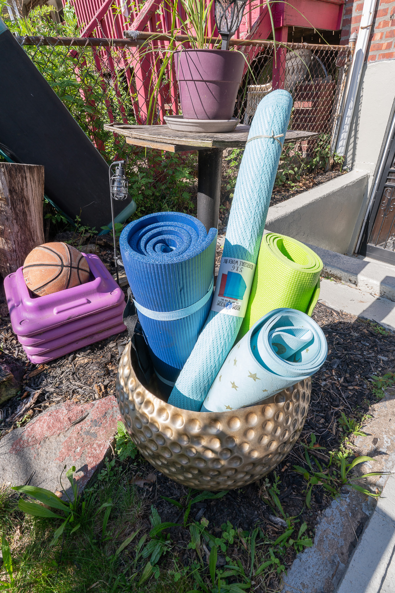 Yoga mats, steppers, and fitness gear stored in a gold basket outdoors